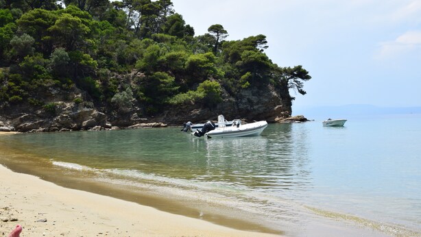 A beach with boats, clear water, and a rocky cliff with trees. - Villa L&M Skiathos (Skiathos)