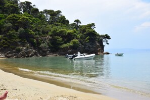 Una playa con barcos, agua cristalina y un acantilado rocoso con árboles.