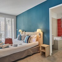 Une chambre d’hôtel avec un lit, des lampes de chevet, une table de nuit, une salle de bain rouge et une vue par la fenêtre.