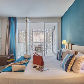 Quarto de hotel com cama, mala, bolsa, mesa com cadeira e varanda com vista.