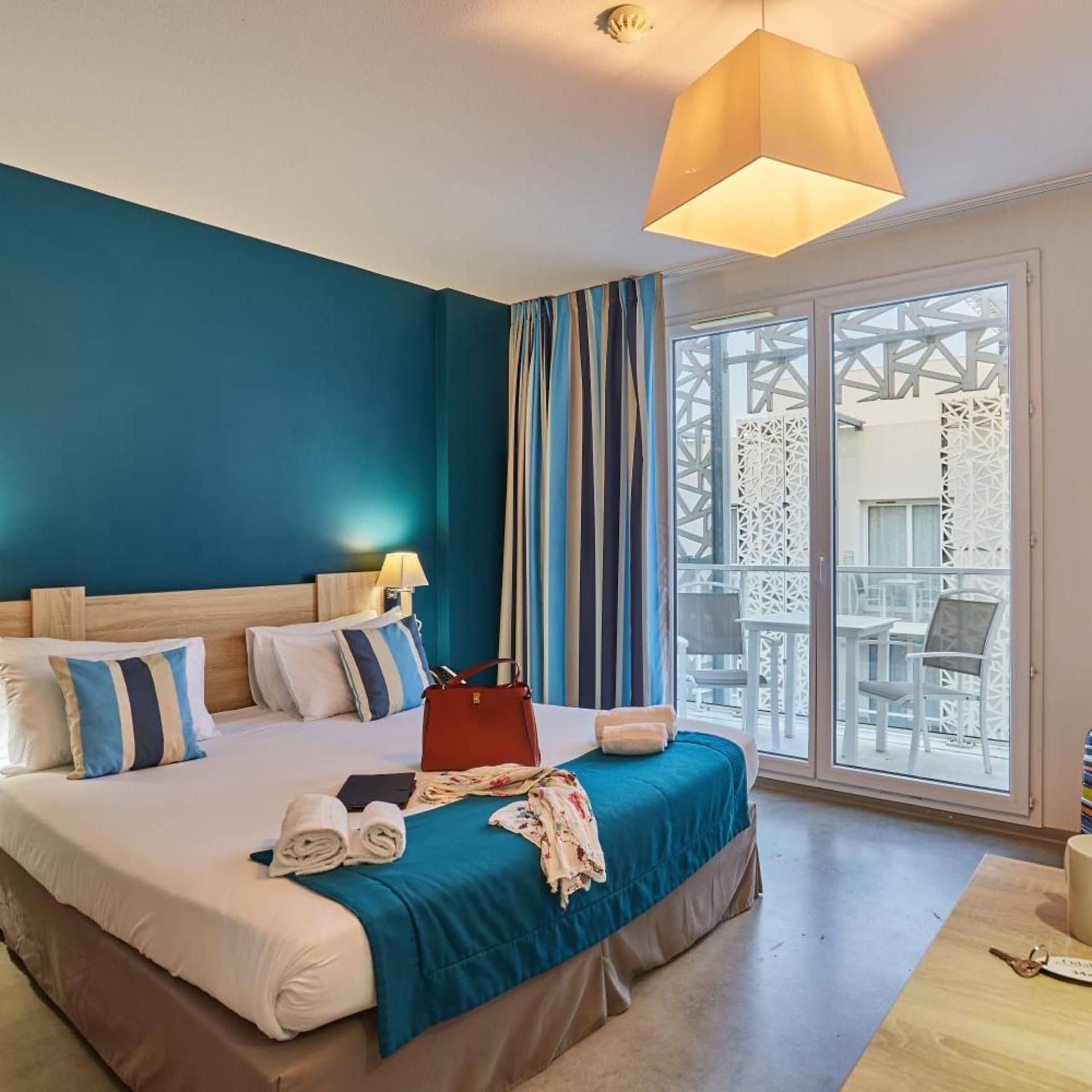 A hotel room with a large bed, a view of the outdoor area, and a balcony with a white railing.
