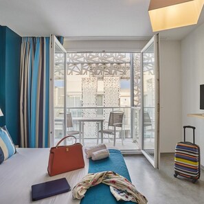 Una habitación de hotel con una cama, una maleta, un bolso y una mesa con sillas.