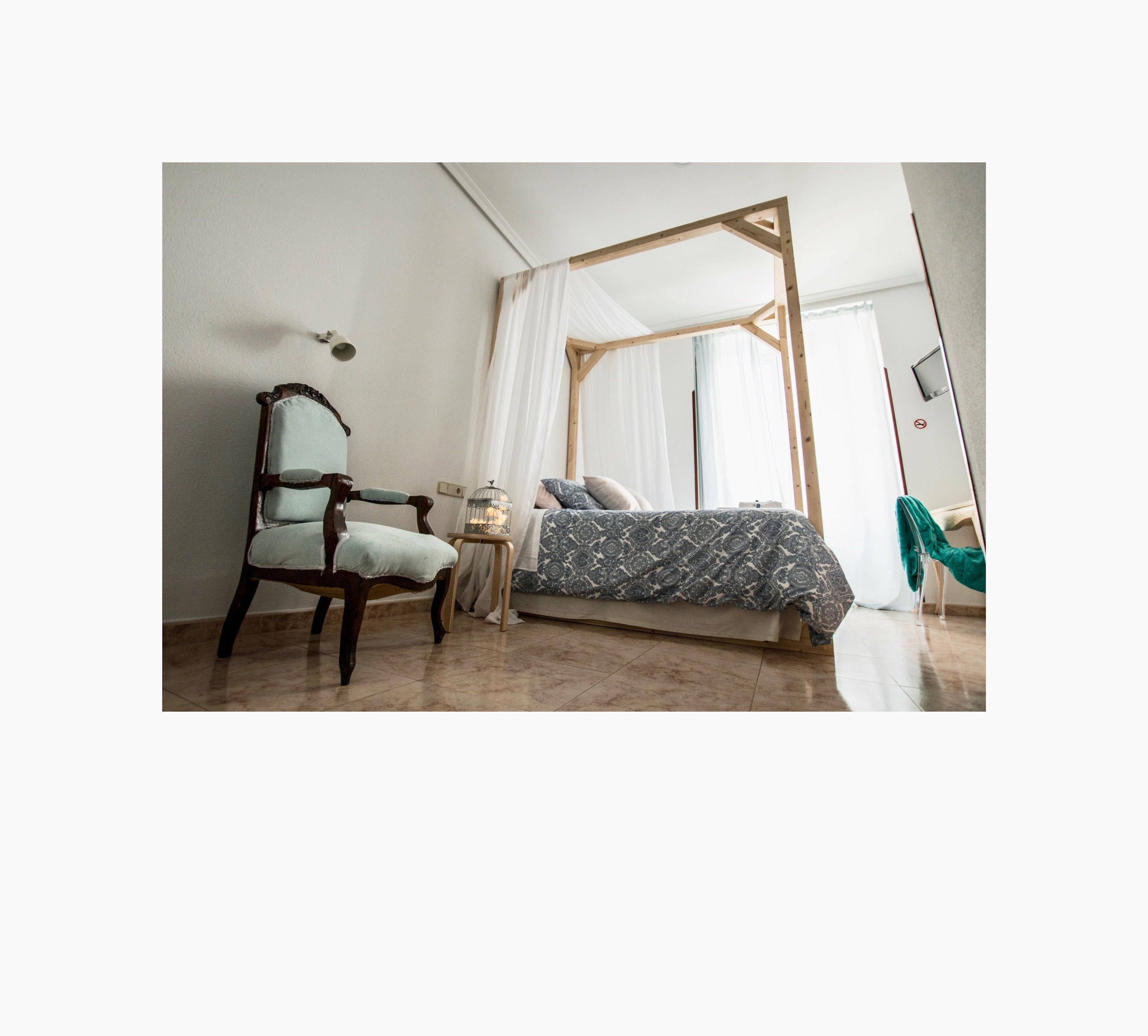 A bedroom with a wooden bed frame, a chair, a small table, and a hanging chair.