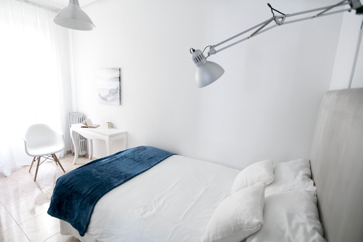 A bedroom with a bed, a desk, a chair, and a desk lamp.
