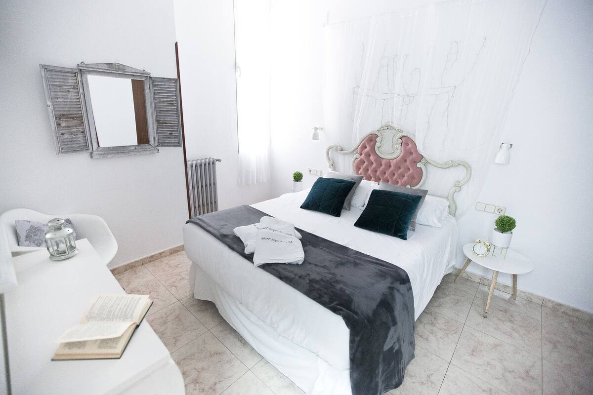 Un dormitorio con una cama, mesitas de noche, una silla, un radiador y una ventana.