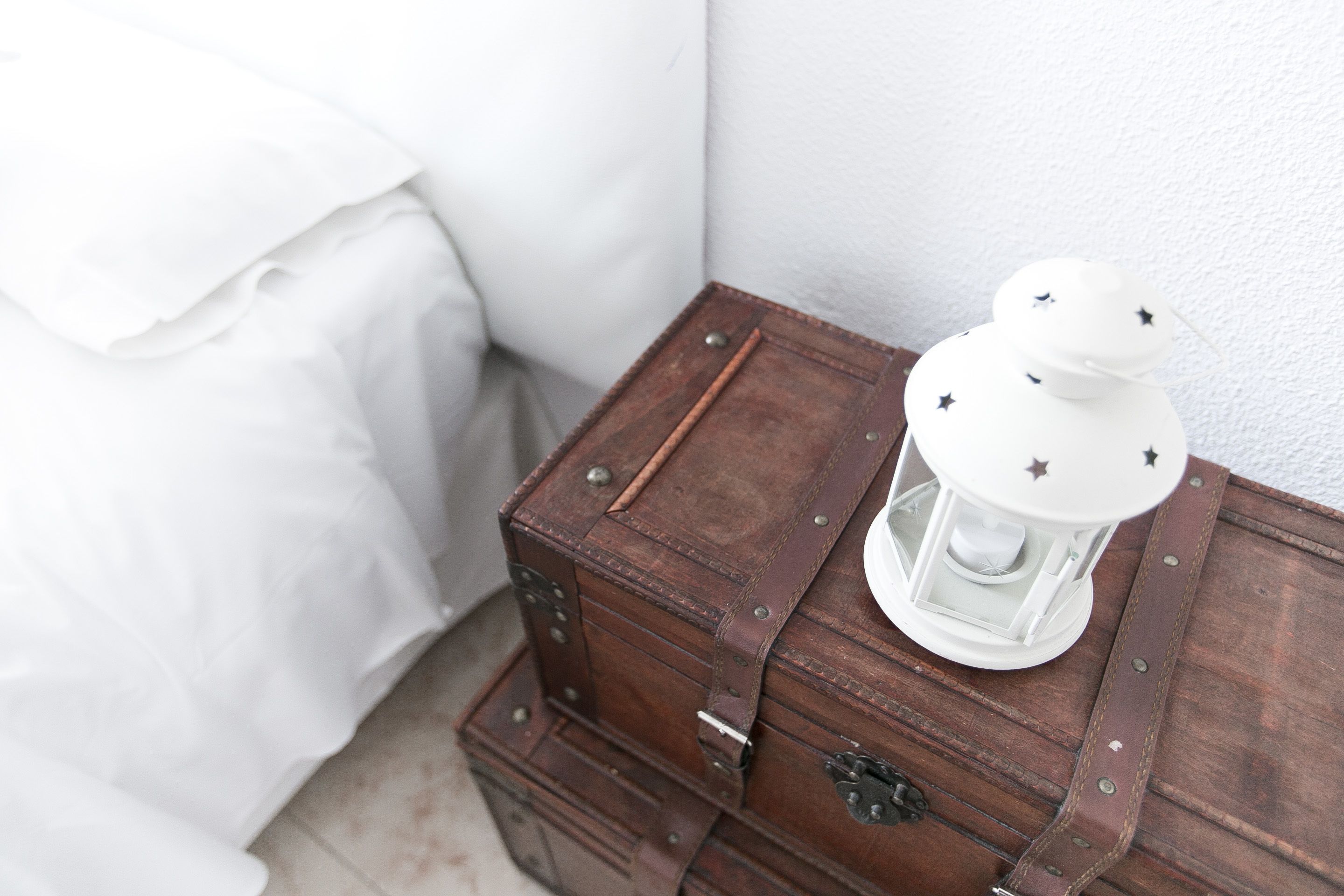 A small, vintage-style wooden chest with a white lantern on top, placed against a white wall.