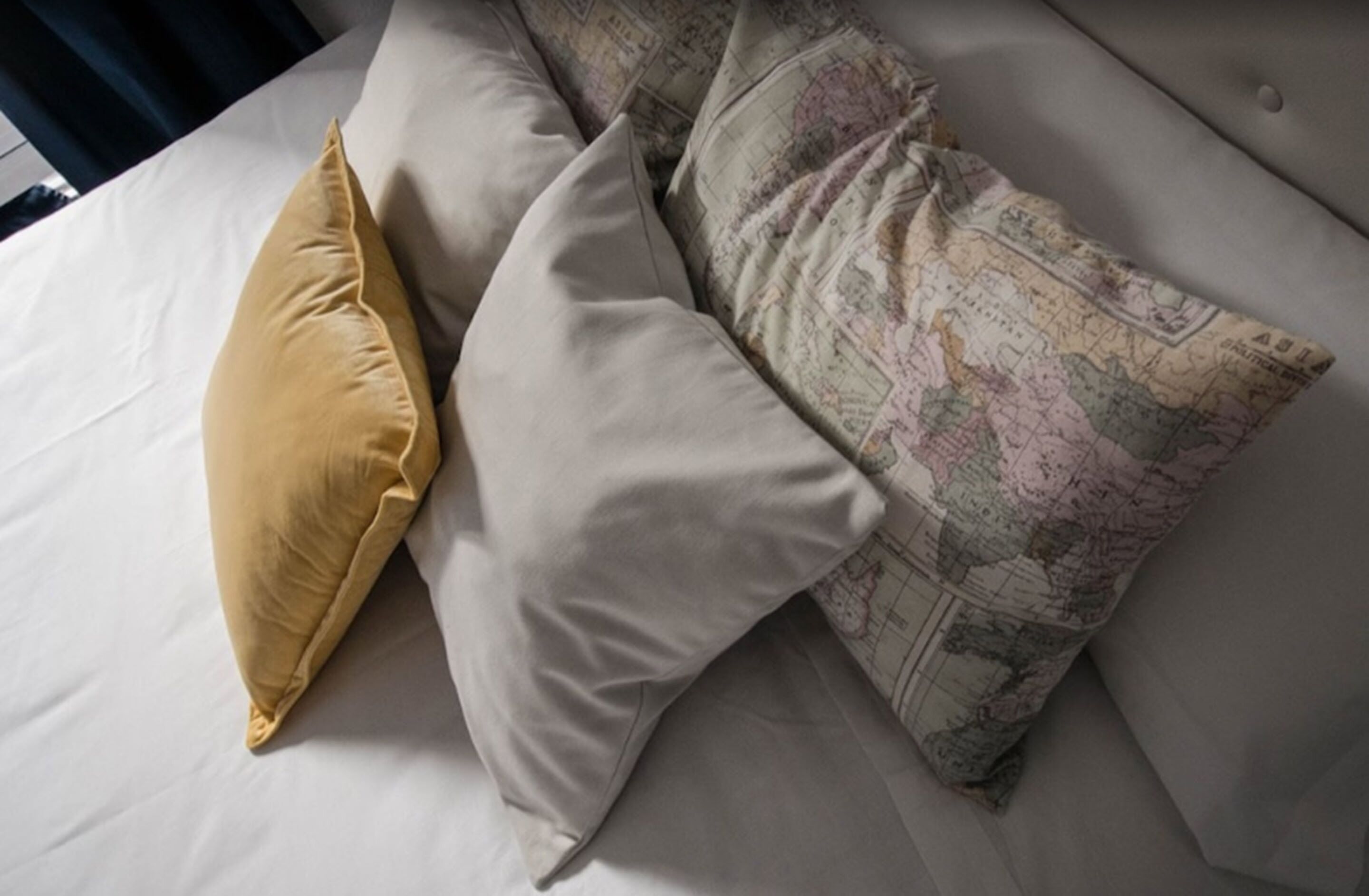 Ein Bett mit weißer Bettwäsche und drei Kissen, eines mit Weltkarten-Muster.
