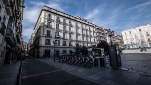 Un edificio histórico de varios pisos, con una fila de bicicletas estacionadas adelante y un cielo azul despejado.