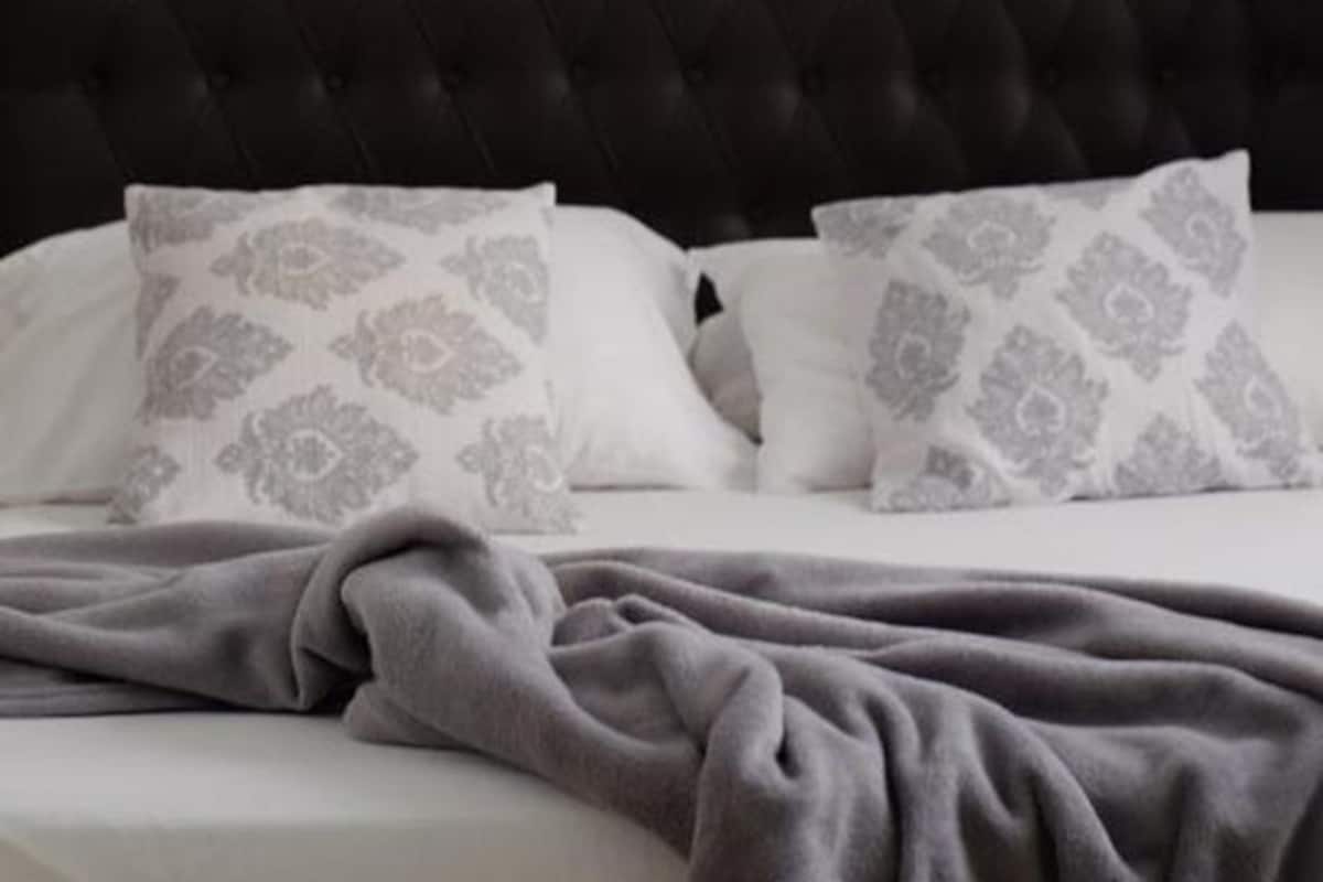 A bed with a dark headboard, two wall-mounted mirrors, and patterned pillows.