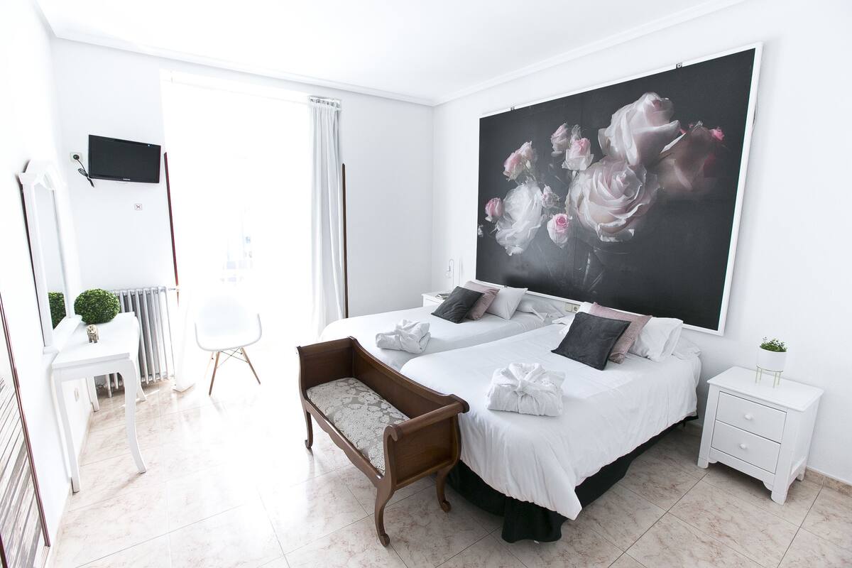 Una habitación de hotel moderna con dos camas, una obra de arte floral grande, una mesita pequeña y una planta en la mesita de noche.