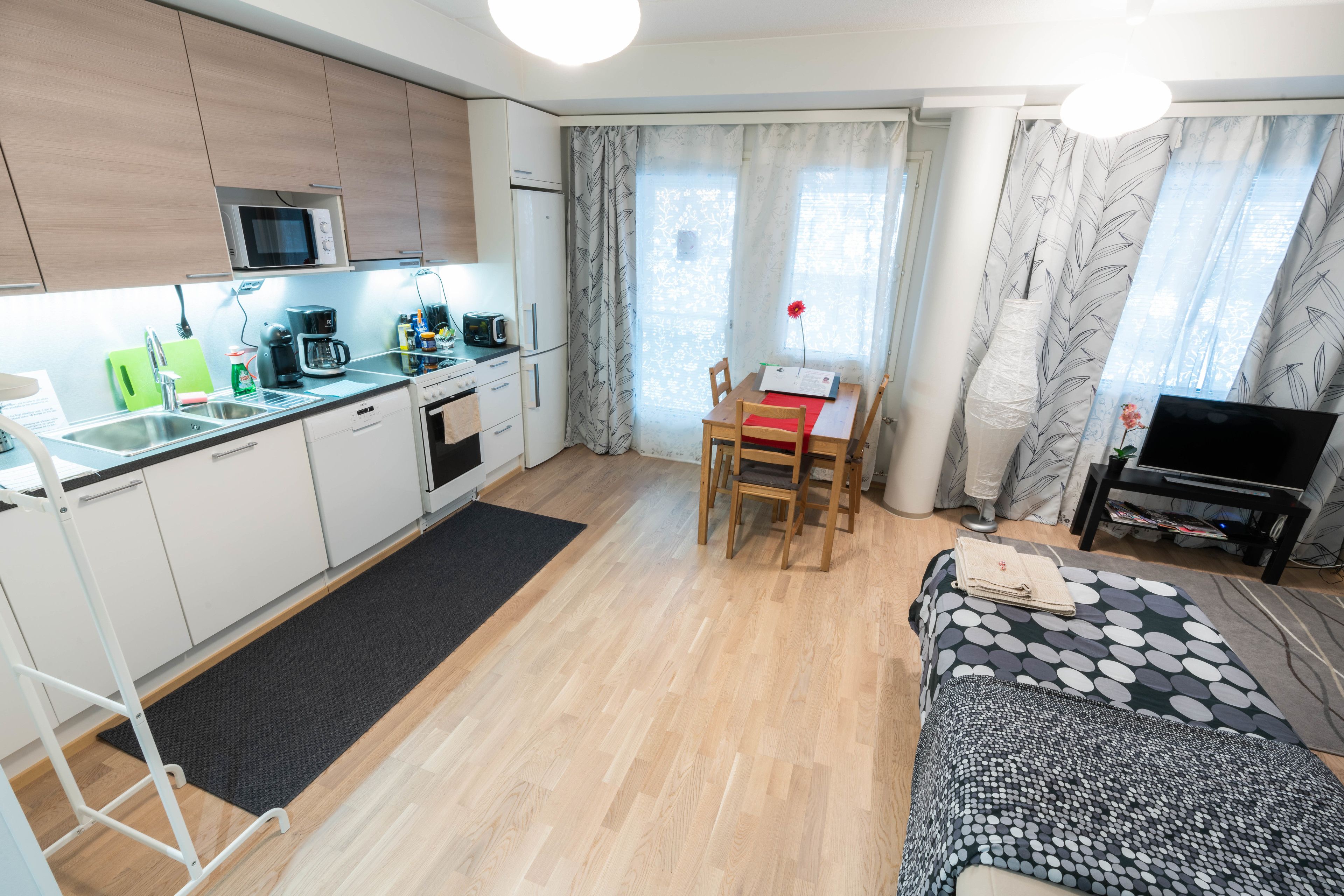 A compact hotel room with a kitchenette, a dining area, and a bed.