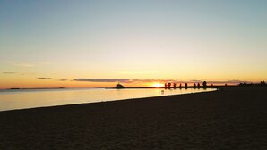 Una playa al atardecer con un mar tranquilo, un muelle y algunas personas caminando por la orilla.