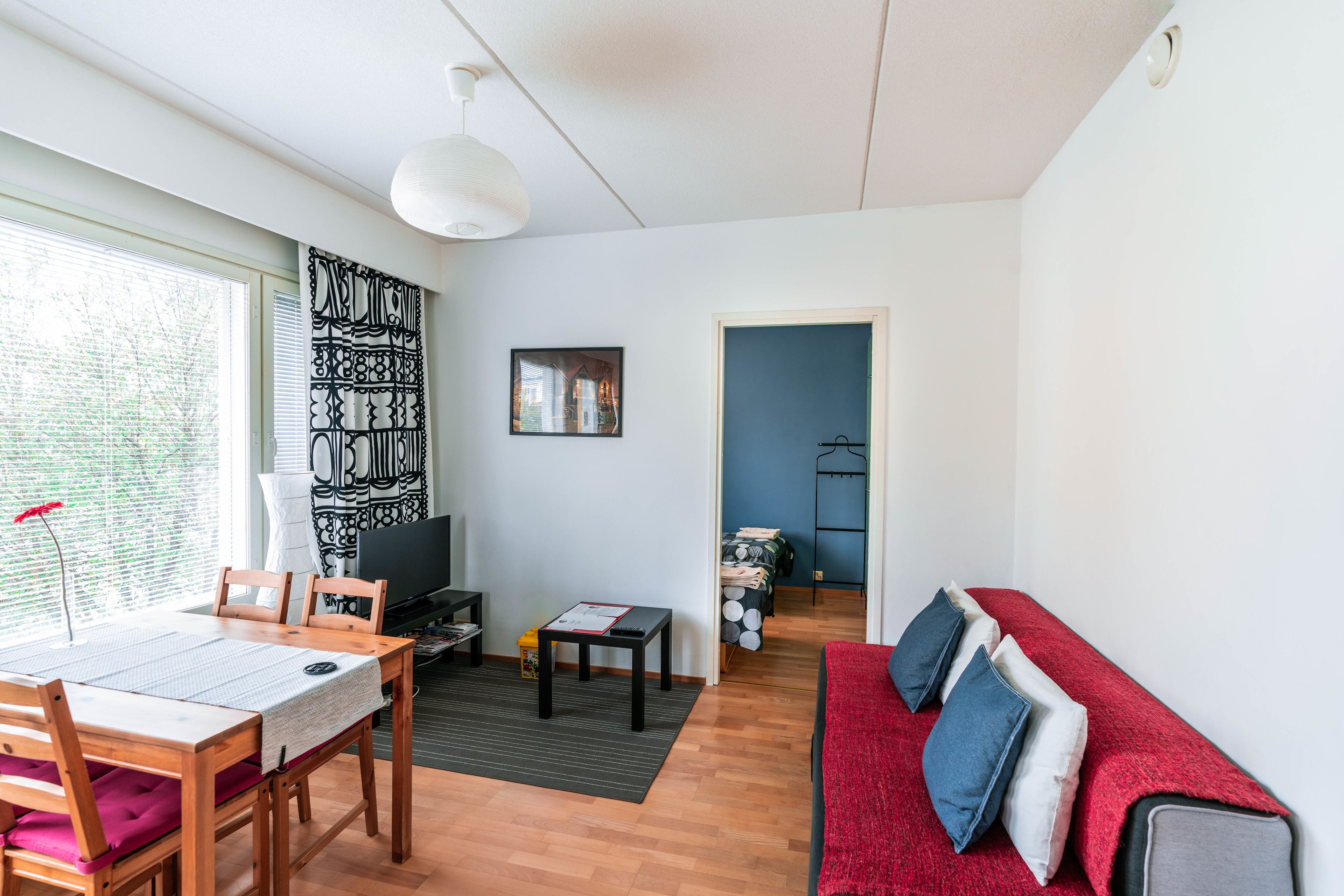 A modern living room with a dining area, a sofa with cushions, a TV, and a bookshelf.