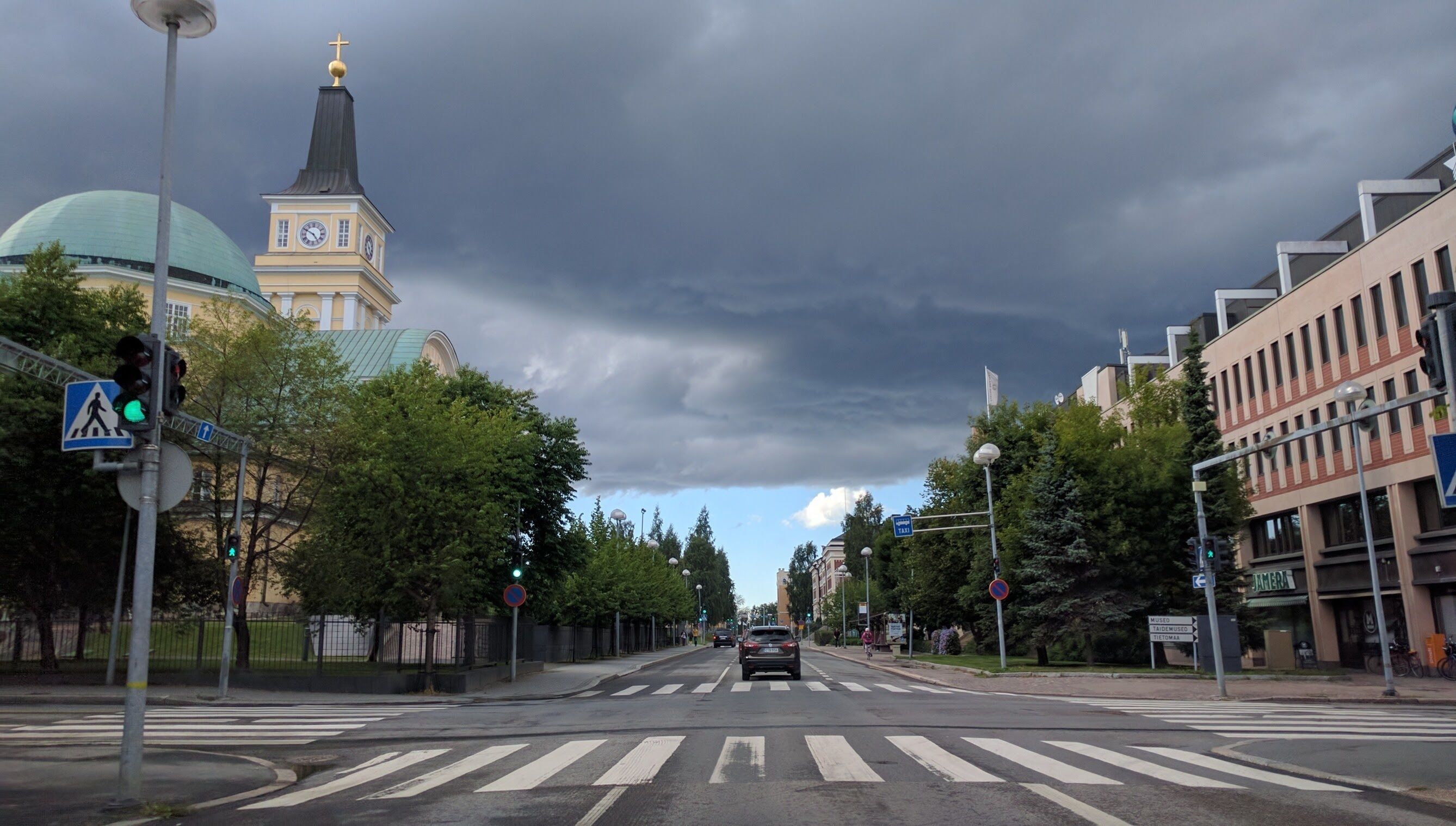 Une vue de rue avec une église, une croix et un bâtiment sur lequel on peut lire l’inscription « JAKIMIA ».