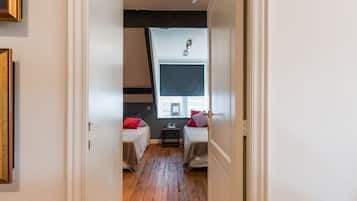 Een smalle gang die leidt naar een slaapkamer met twee bedden, een tafeltje en een raam met uitzicht.