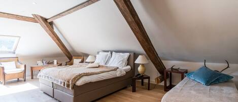 A bedroom with a sloped ceiling, a bed, a chair, a small table, and a lamp.