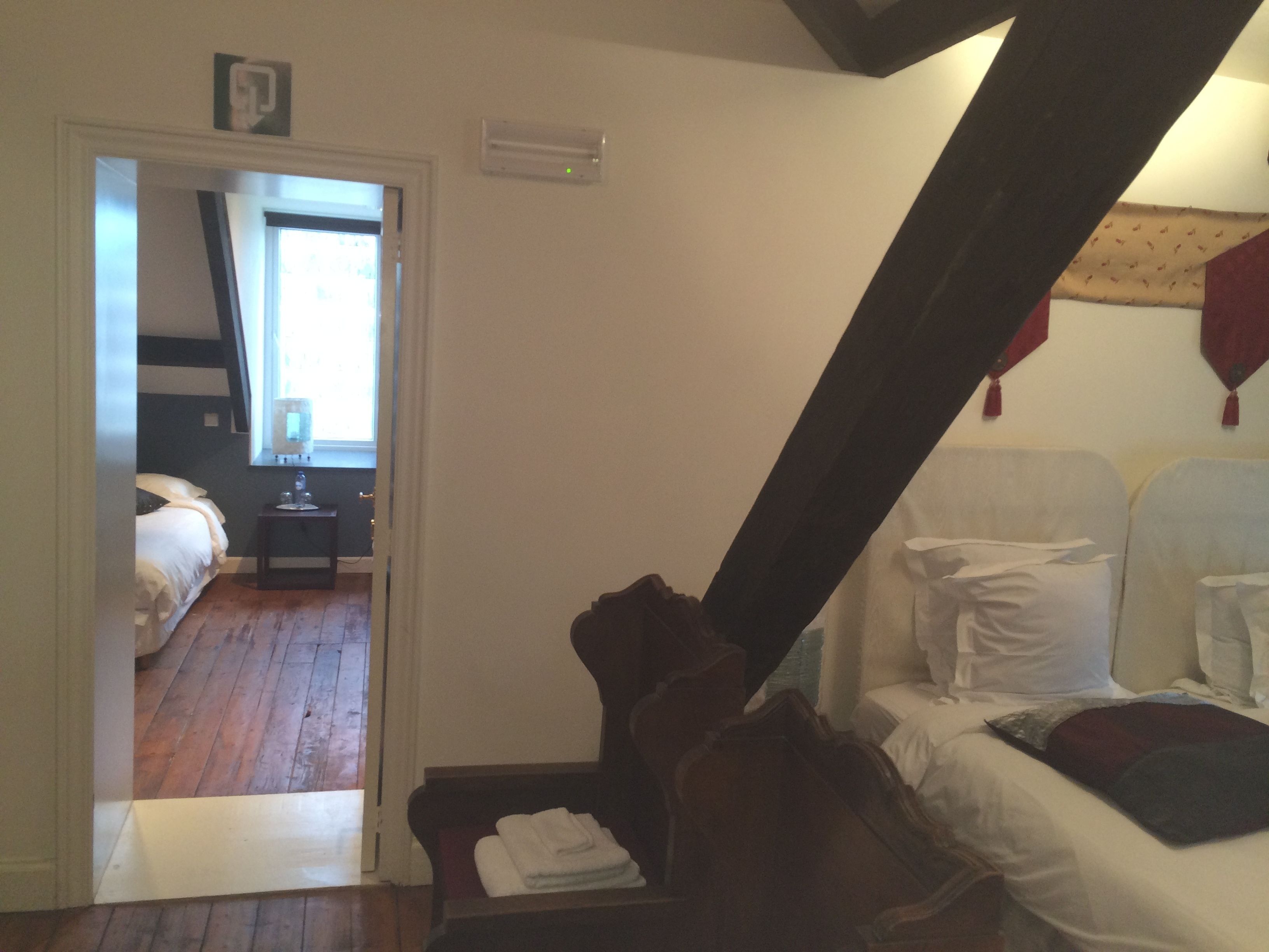 Une chambre avec un plancher en bois, un lit avec une literie blanche, une table de chevet avec une lampe et une fenêtre avec des rideaux.