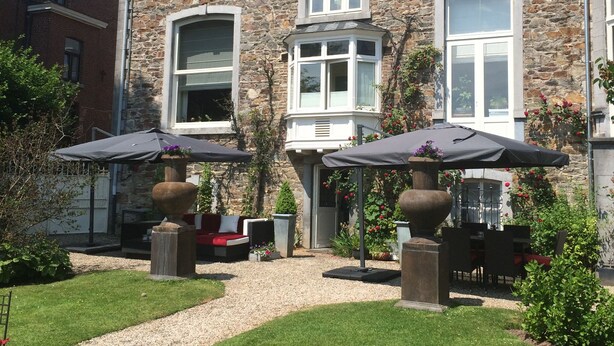 A stone building with multiple windows and a paved patio area with outdoor furniture and umbrellas. - Hotel Dufays (Stavelot)