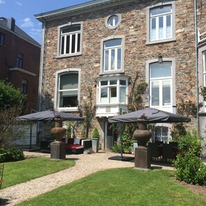 A stone building with multiple windows and a paved patio area with outdoor furniture and umbrellas. - Hotel Dufays (Stavelot)