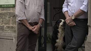 Dois homens em frente a um edifício, com um cão.