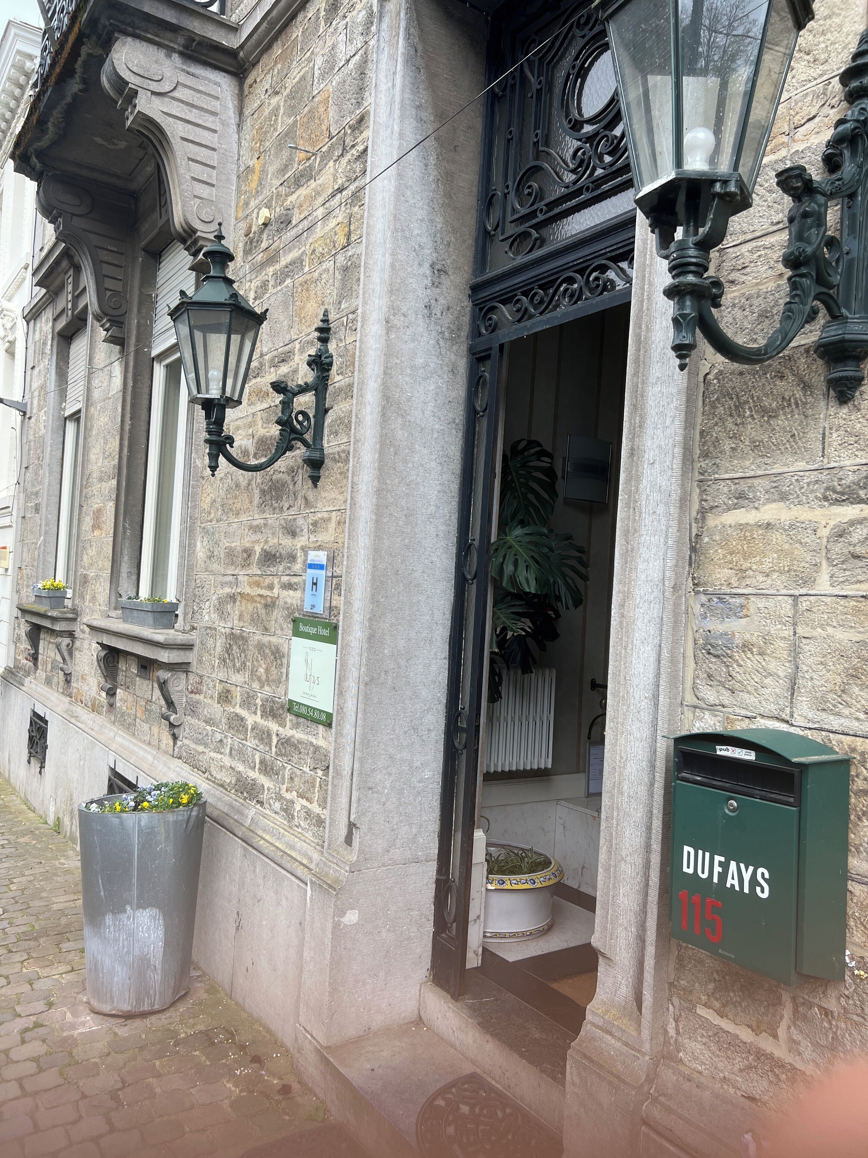 A stone building with a boutique hotel sign, a green mailbox, and a trash bin.