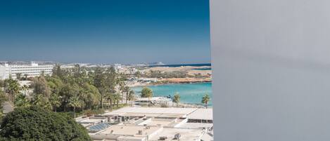 A view of a coastal area with a building featuring a rooftop parking area and solar panels, overlooking a beach and the sea.