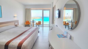 Habitación de hotel con una cama grande, un escritorio, una silla y vista al mar.