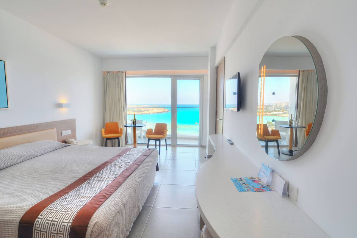 Een hotelkamer met een groot bed, een bureau, een stoel en uitzicht op zee.