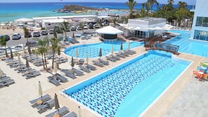 Un resort con varias piscinas, tumbonas y vista al océano.