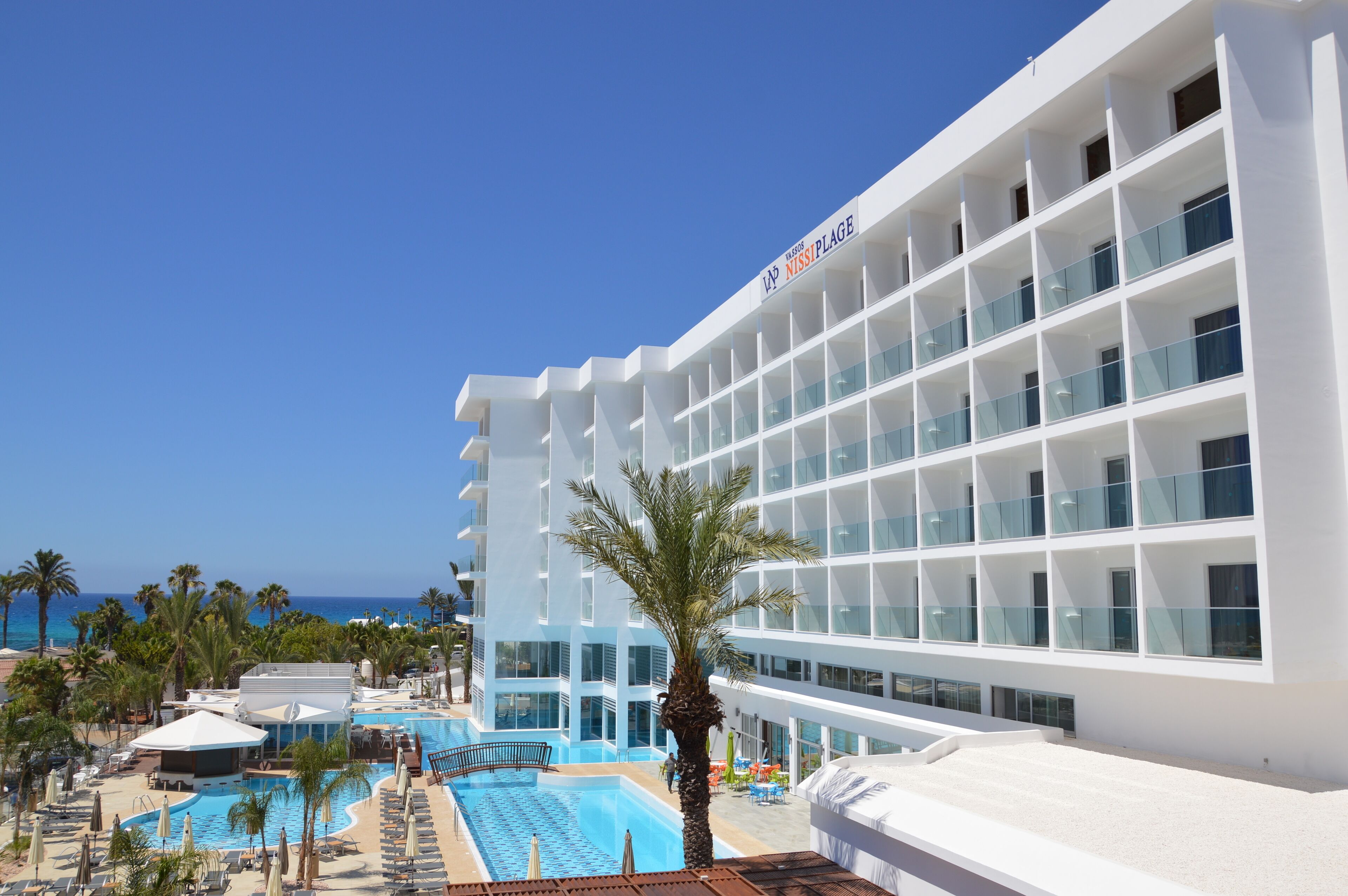 Un hotel moderno con zona de piscina, palmeras y una vista despejada del océano.