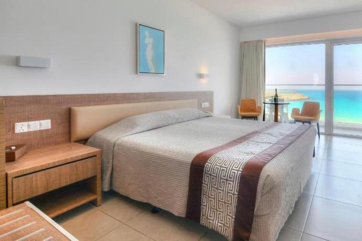 Une chambre d’hôtel avec un lit, un bureau, une chaise, une petite table et une vue sur l’océan.