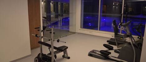 Un gimnasio moderno con una máquina de remo, un banco de pesas y una cinta de correr.