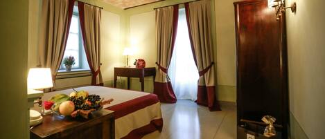 Une chambre d’hôtel avec un lit, un bureau doté d’une lampe, une petite table avec un vase et une poubelle.
