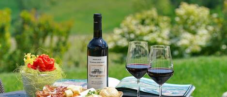 A table with a bottle of wine, two glasses of red wine, a cheese board, bread, and a bouquet of flowers.