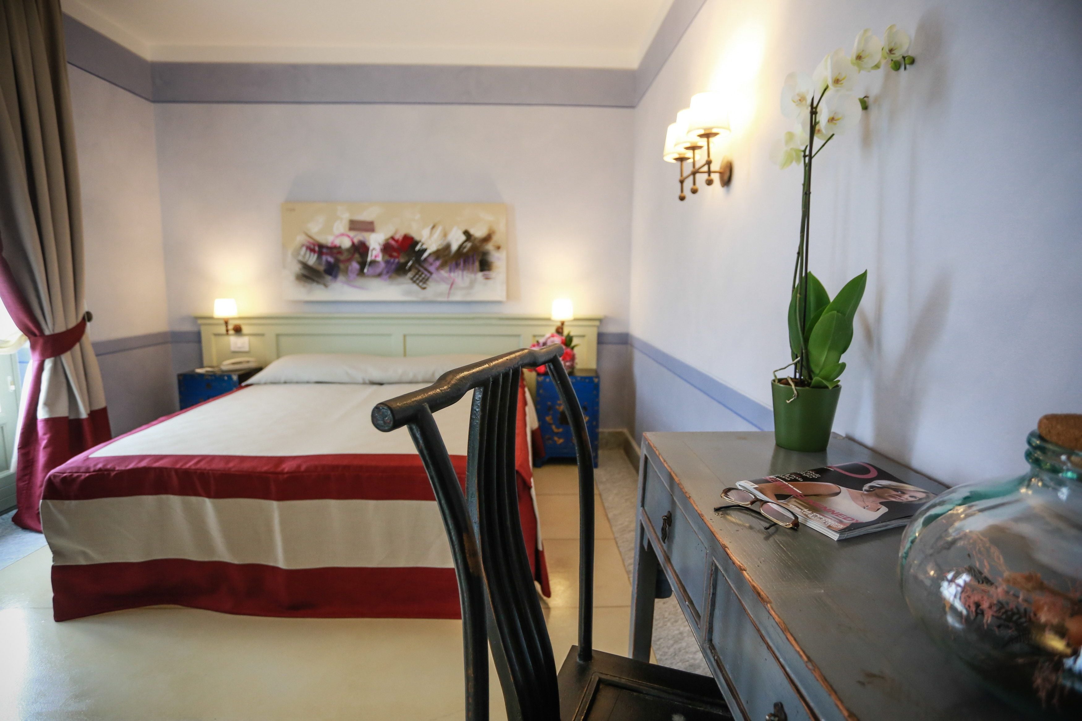 A hotel room with a bed, a nightstand, a lamp, a potted orchid, and a magazine on the side table.