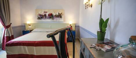 A hotel room with a bed, a nightstand, a lamp, a potted orchid, and a magazine on the side table.