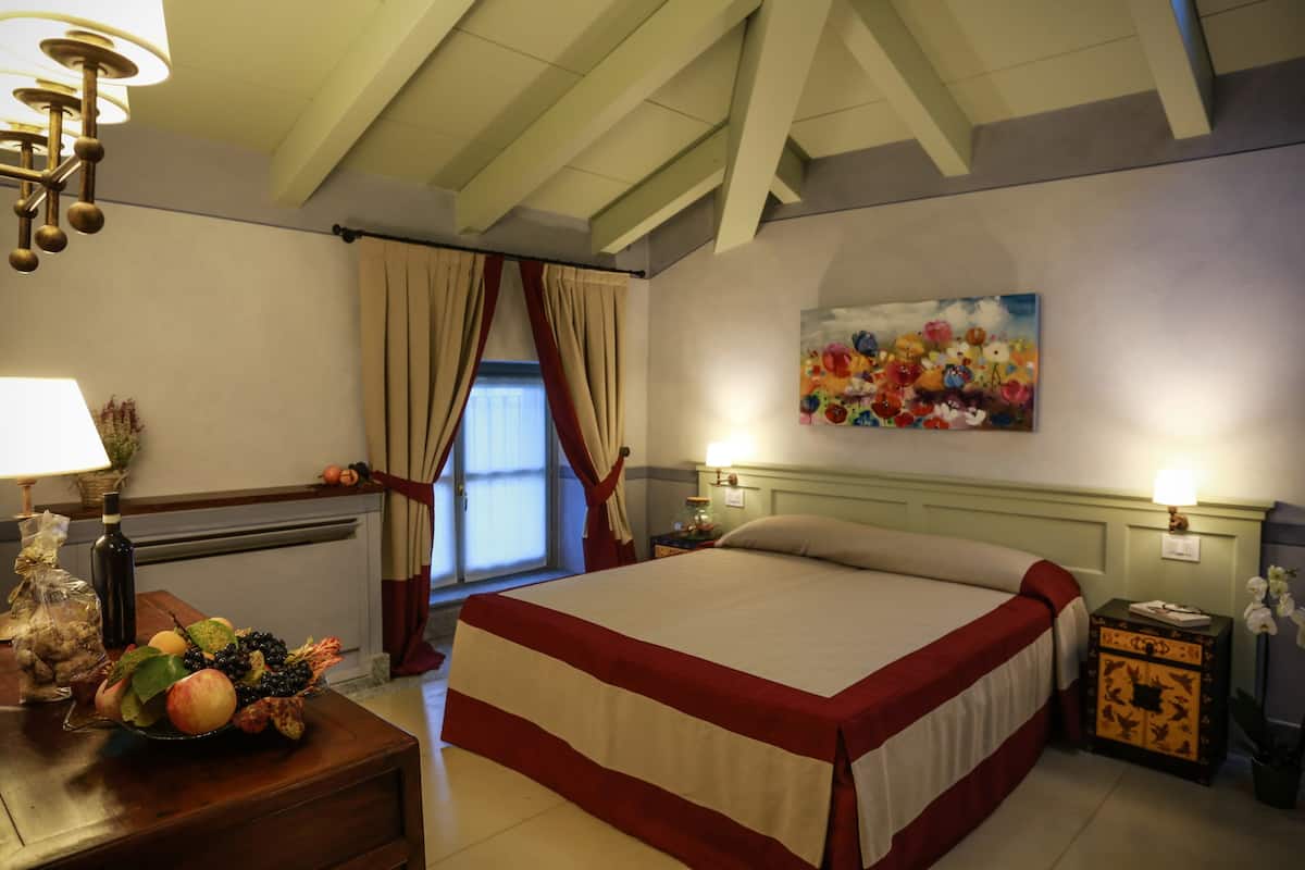 Une chambre d’hôtel avec un grand lit, un tableau au mur, une table de chevet avec une lampe et une fenêtre avec des rideaux.