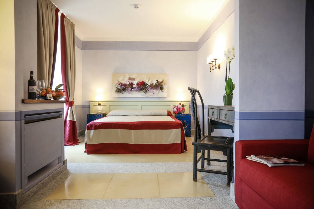 Une chambre d’hôtel avec un lit, un bureau, une chaise, une télévision et une fenêtre avec des rideaux.