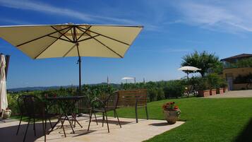 Een terras buiten met een tafel en stoelen, een grote parasol en uitzicht op het landschap.
