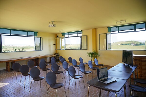 Un aula con un proyector, una computadora portátil y un televisor sobre una mesa. Hay sillas dispuestas alrededor de la habitación y un banco a lo largo de una pared.