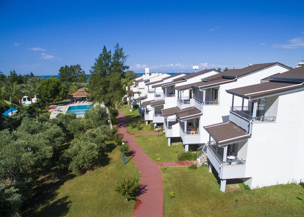 A row of white buildings with balconies, a swimming pool, and a red pathway.