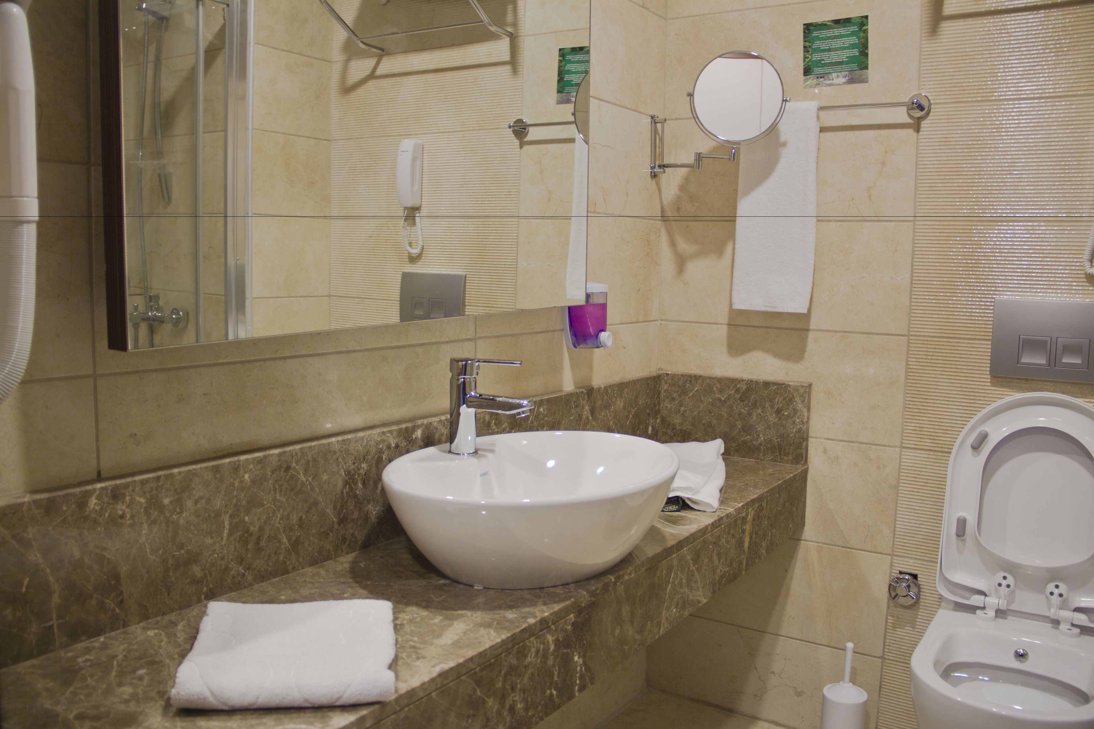 A bathroom with a marble sink, a mirror, a toilet, and a hand dryer.