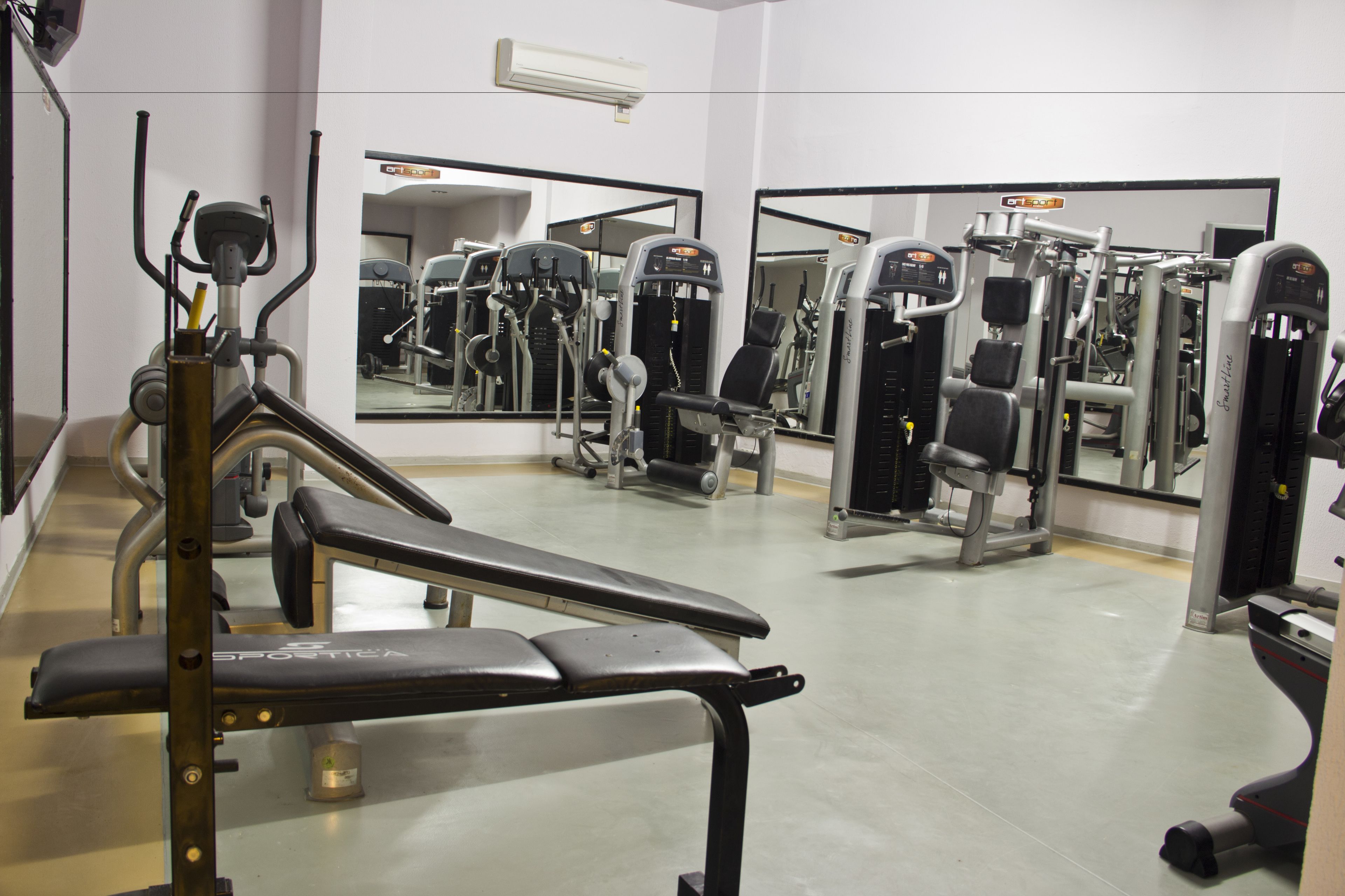 A gym with various exercise machines, a bench, and mirrors on the walls.