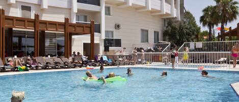 A swimming pool with people, a building with balconies, and a palm tree.