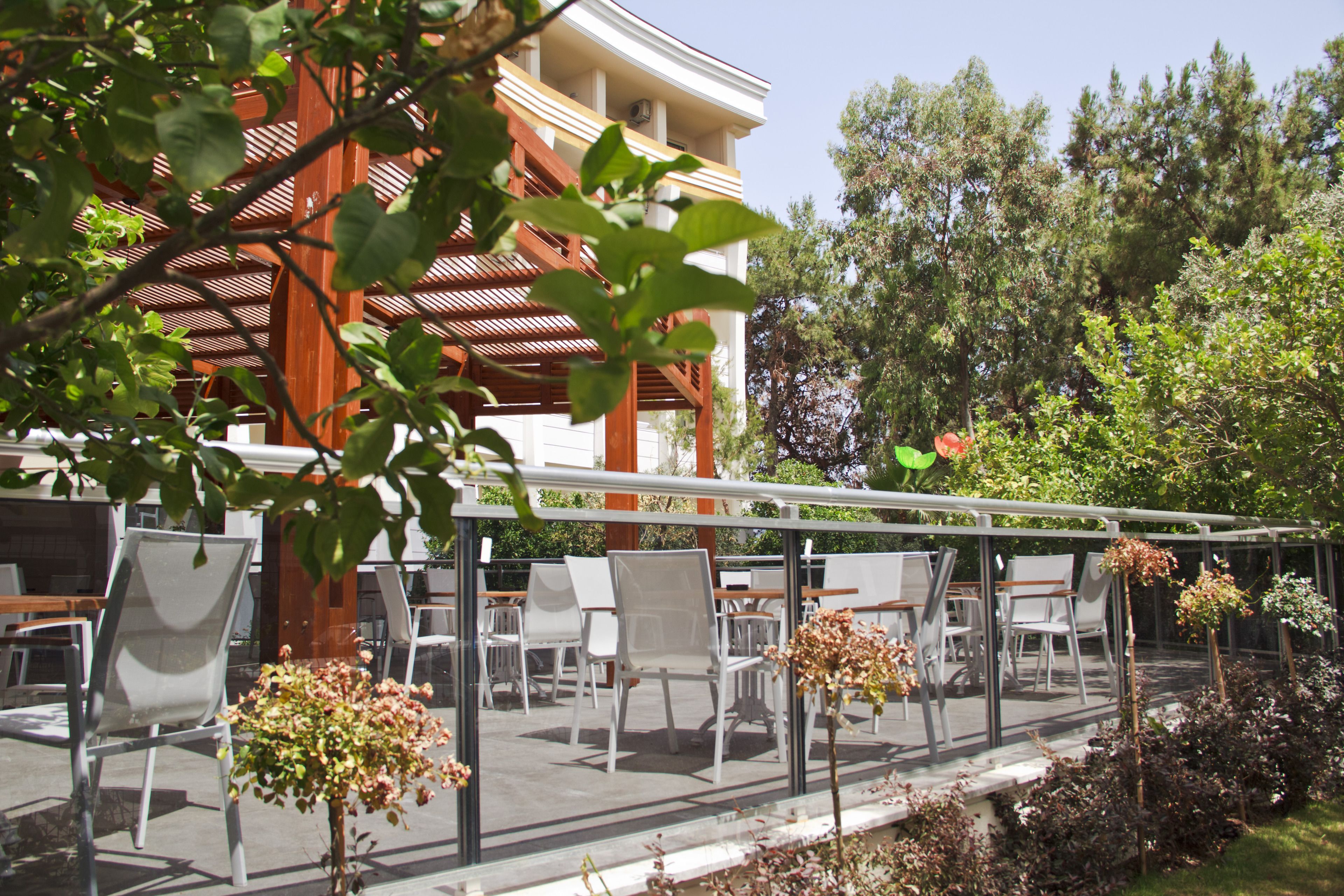 An outdoor seating area with tables and chairs, a wooden pergola, and a view of a building with columns.