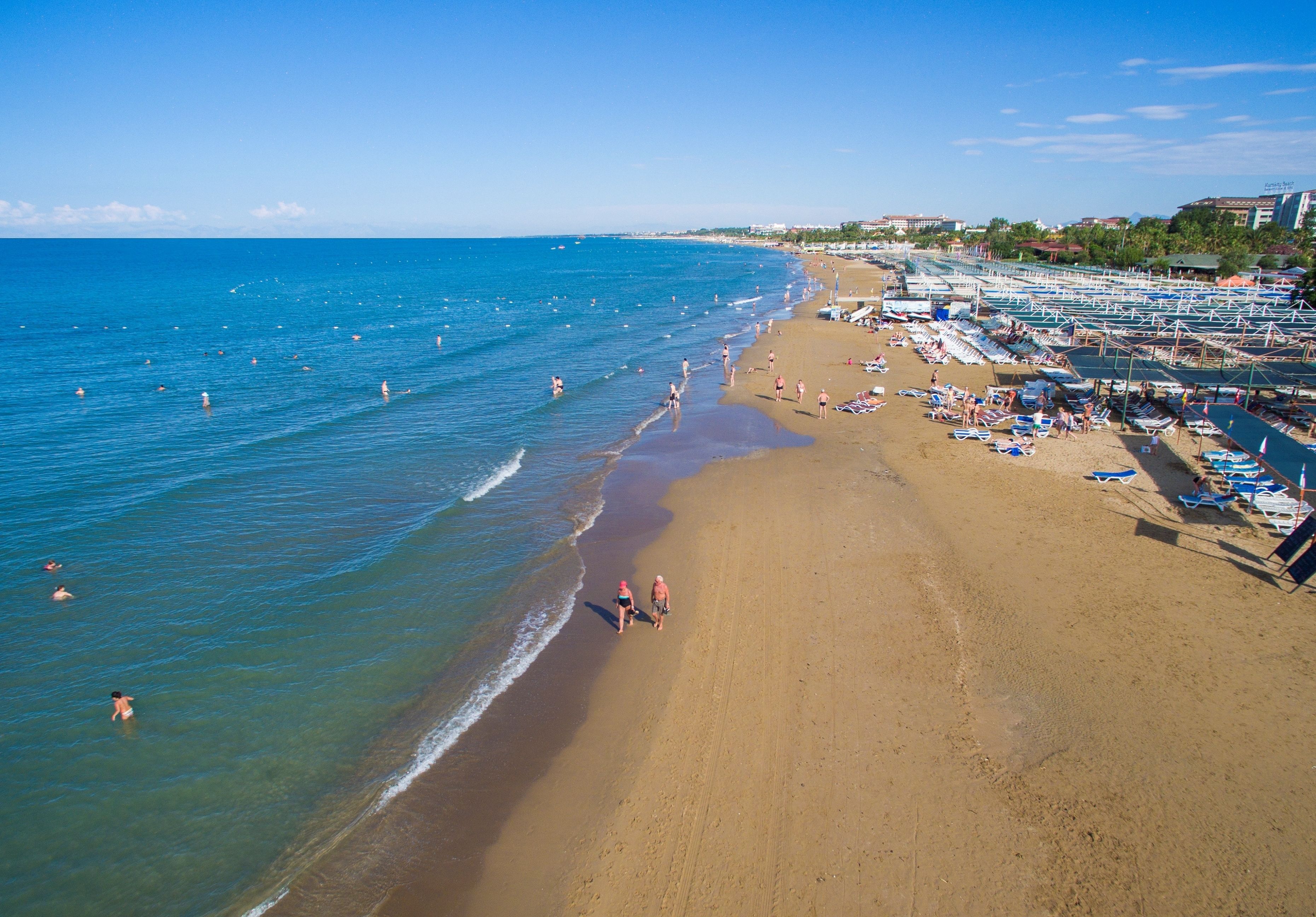 A beach with clear blue water, a sandy shore, and several beach umbrellas and lounge chairs.