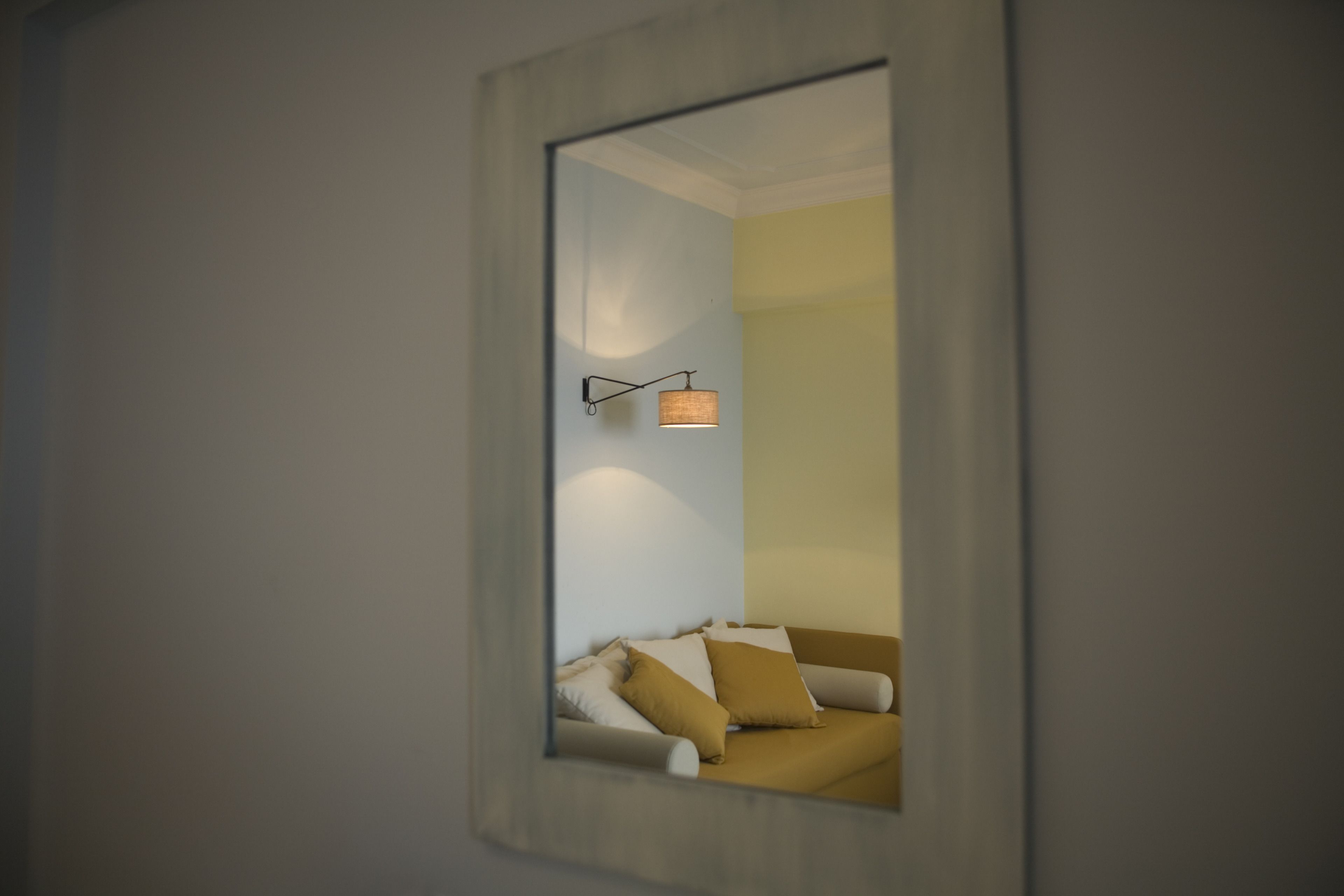 Une chambre moderne avec un grand miroir qui reflète un canapé et une lampe fixée au mur.