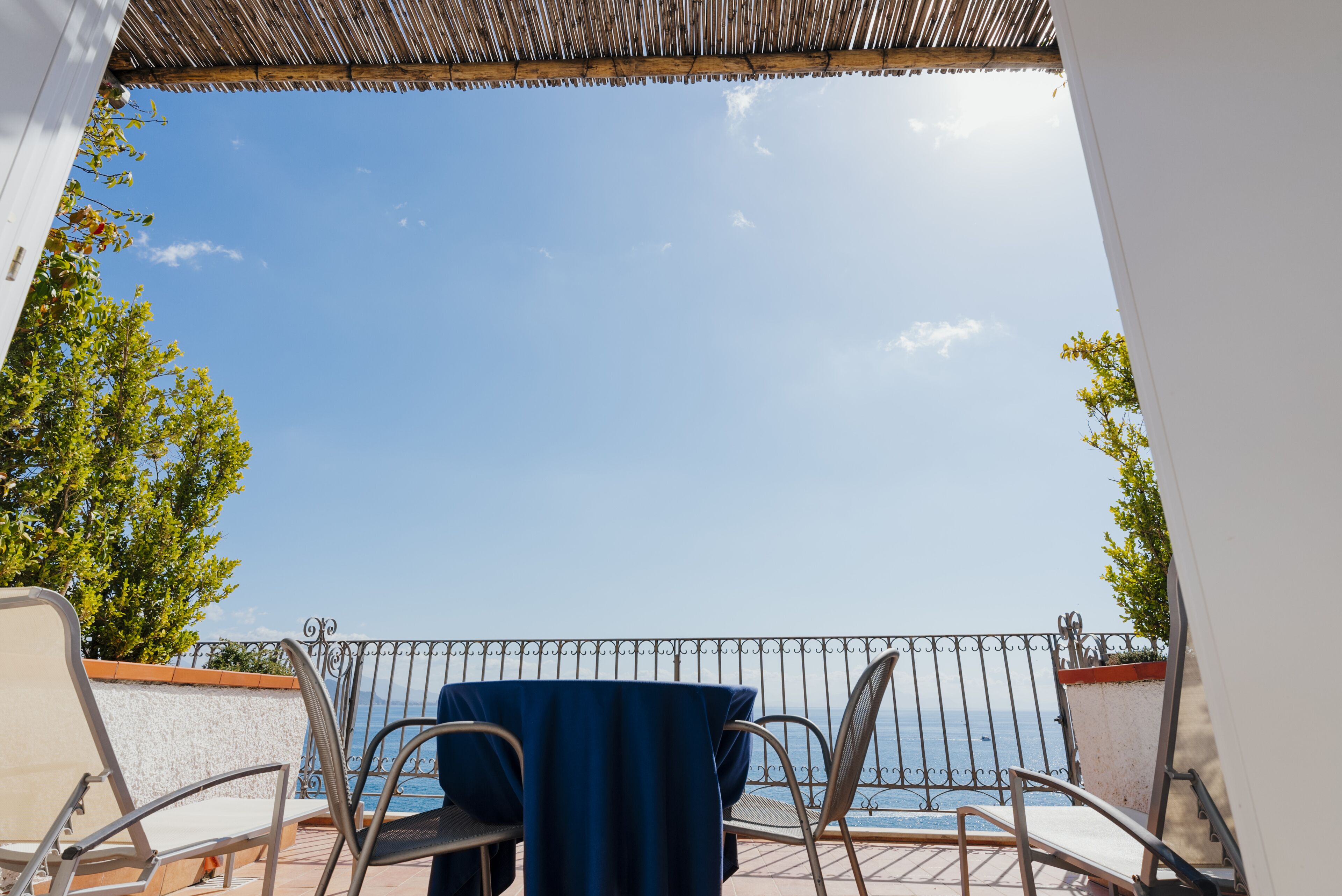 A balcony with a table and chairs, overlooking a clear blue sky and a body of water.