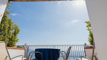 Un balcone con tavolo e sedie, vista su un cielo azzurro e un tratto d'acqua.