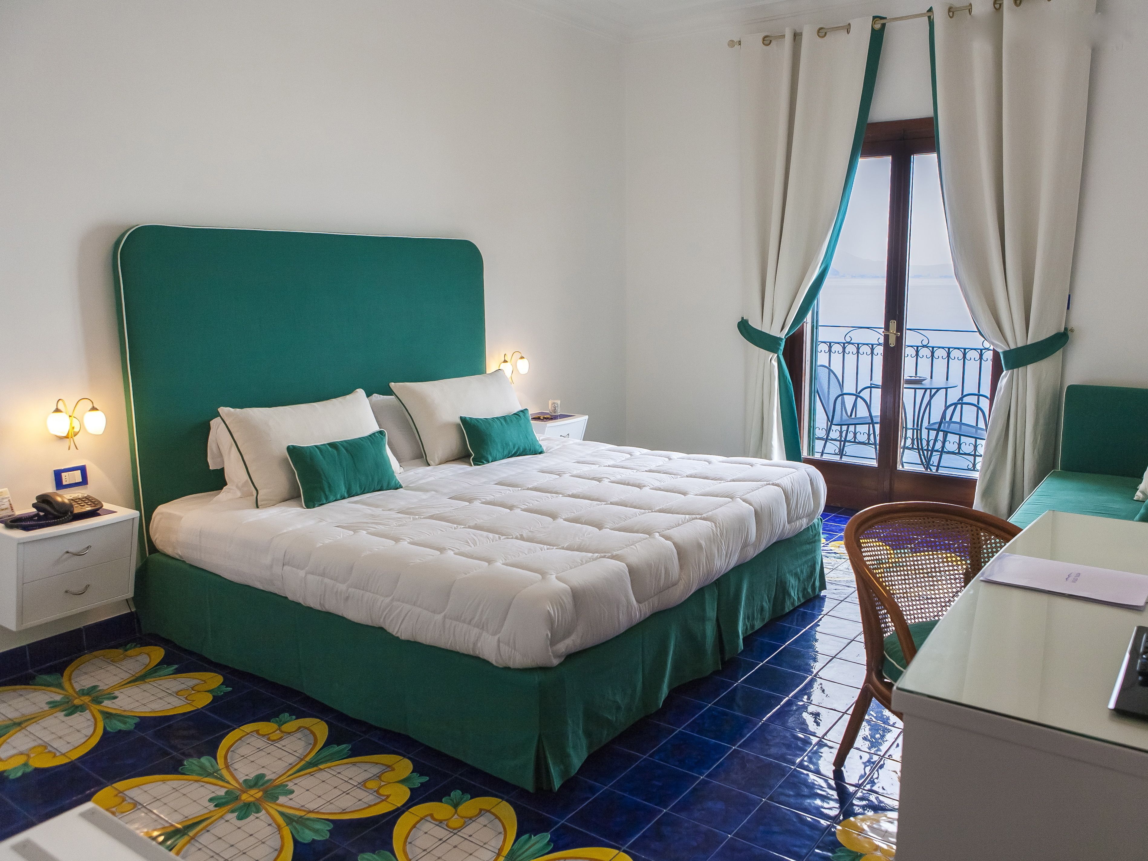 A hotel room with a bed, a desk, a chair, a nightstand, and a window with curtains.
